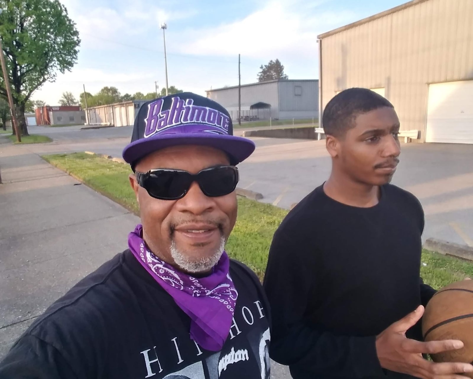 Jon Mic standing outdoors with his son, who is holding a basketball.